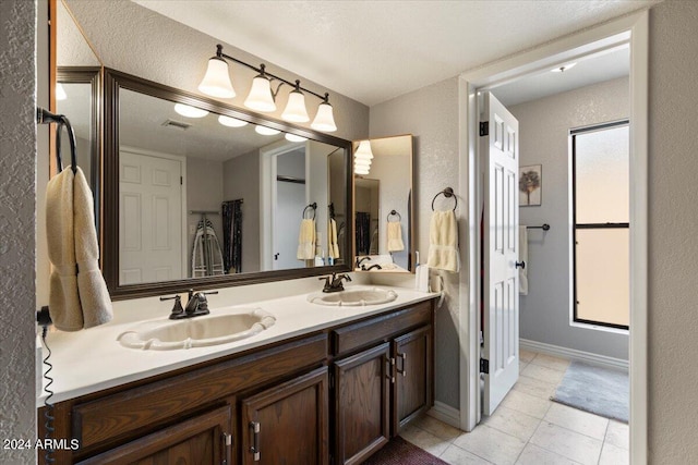 bathroom with a textured wall, visible vents, a sink, and double vanity