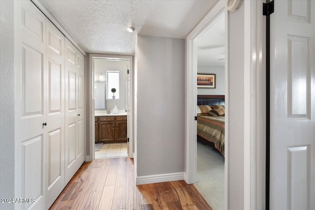 hall with a textured ceiling, a textured wall, light wood-style flooring, and baseboards