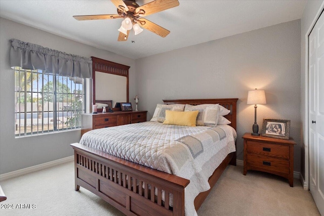 bedroom with light carpet, ceiling fan, a closet, and baseboards