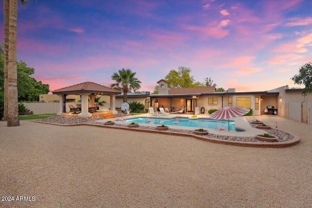 pool at dusk featuring a gazebo, a patio, fence, and an outdoor pool