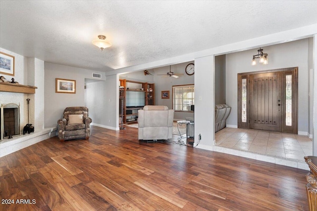 entrance foyer featuring a textured ceiling, visible vents, a fireplace with raised hearth, and wood finished floors