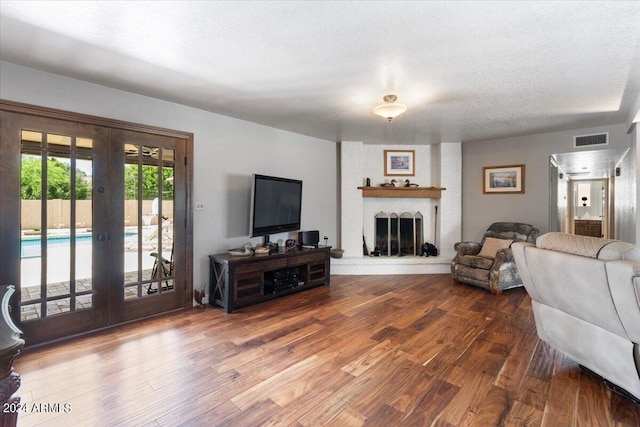 living area featuring visible vents, wood finished floors, a textured ceiling, french doors, and a fireplace