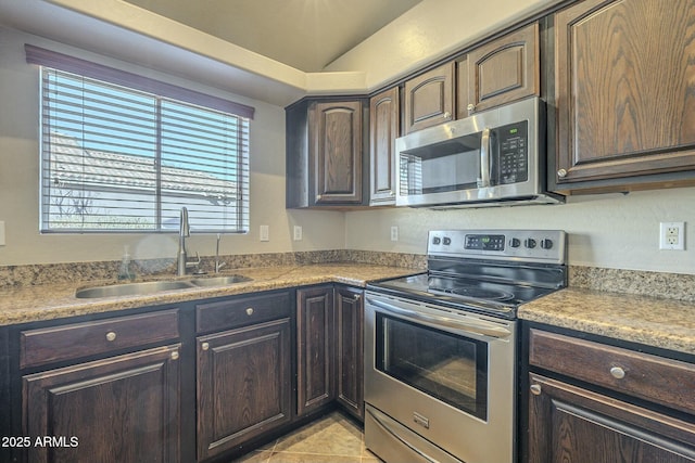 kitchen with dark brown cabinetry, sink, light tile patterned floors, and stainless steel appliances