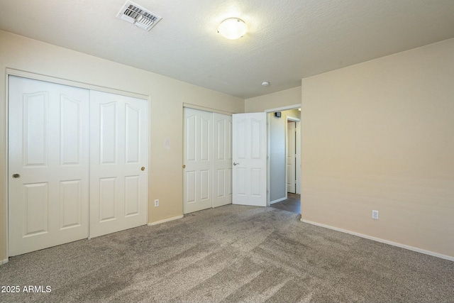 unfurnished bedroom featuring a textured ceiling, multiple closets, and carpet flooring