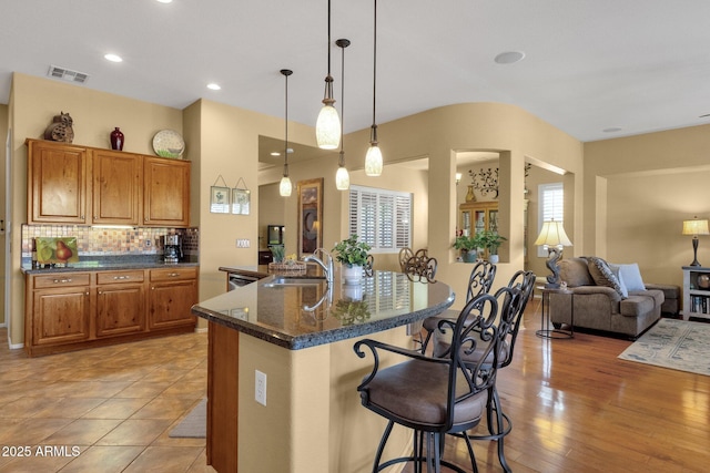 kitchen featuring a sink, brown cabinets, a kitchen breakfast bar, visible vents, and open floor plan