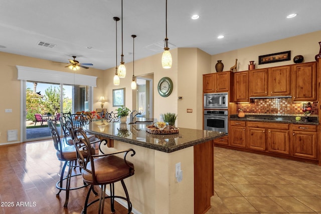 kitchen featuring brown cabinets, a sink, decorative backsplash, visible vents, and appliances with stainless steel finishes
