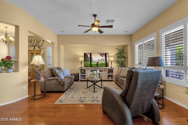 living area featuring baseboards, visible vents, wood finished floors, and ceiling fan with notable chandelier