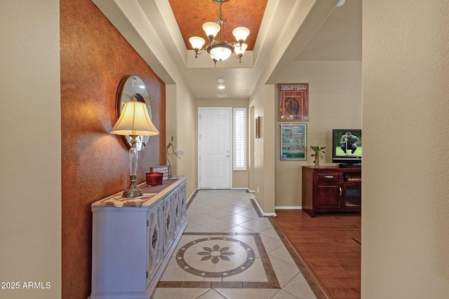 entrance foyer with baseboards, light tile patterned floors, a raised ceiling, and an inviting chandelier