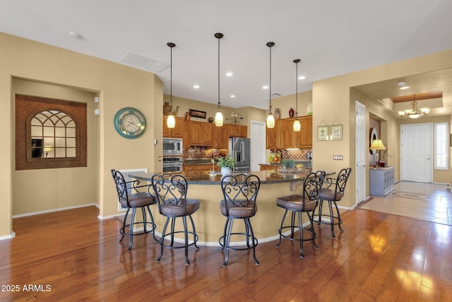 kitchen with brown cabinets, decorative backsplash, a breakfast bar area, hardwood / wood-style floors, and appliances with stainless steel finishes