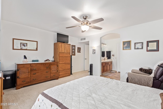 bedroom featuring visible vents, arched walkways, a ceiling fan, light colored carpet, and ensuite bath