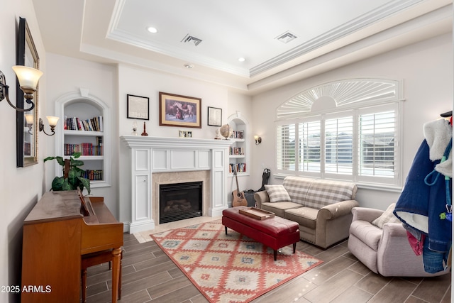 living room with a raised ceiling, ornamental molding, built in features, and a fireplace