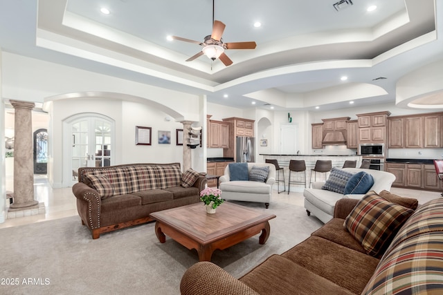 living room with a raised ceiling, ceiling fan, and ornate columns