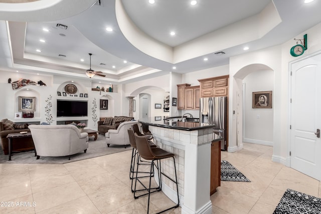 kitchen featuring a breakfast bar area, stainless steel fridge, a raised ceiling, and a center island with sink