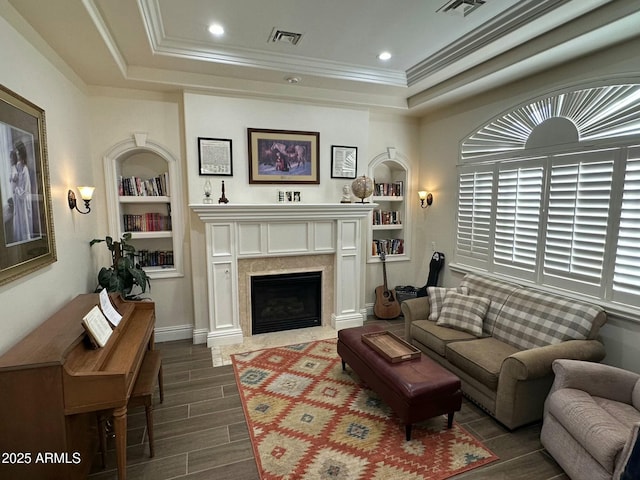 living room with crown molding, a tray ceiling, built in features, and a premium fireplace