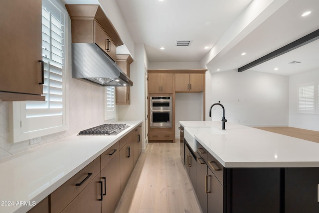 kitchen featuring stainless steel appliances, a sink, visible vents, light countertops, and light wood finished floors