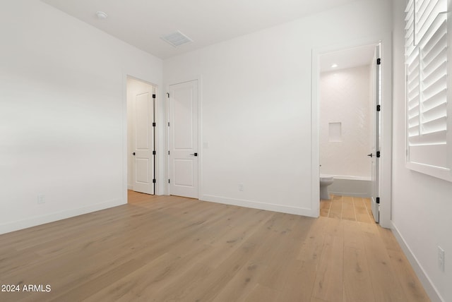 unfurnished bedroom with visible vents, ensuite bath, light wood-style flooring, and baseboards