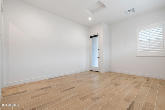 unfurnished room with attic access, light wood-type flooring, visible vents, and baseboards