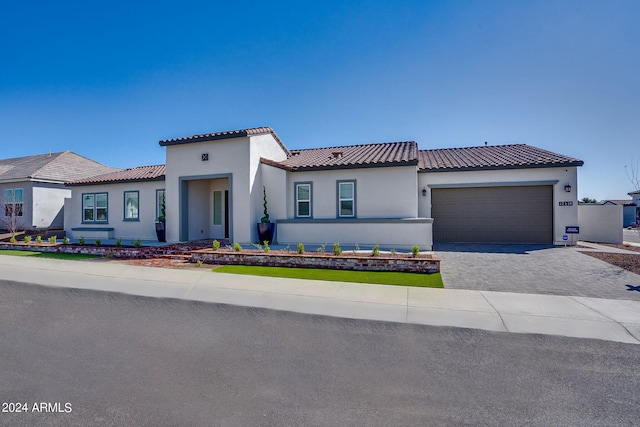 mediterranean / spanish house featuring an attached garage, a tile roof, decorative driveway, and stucco siding