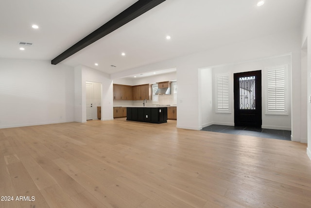 unfurnished living room featuring vaulted ceiling with beams, recessed lighting, a sink, baseboards, and light wood finished floors