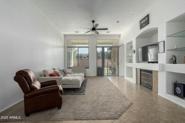 living area featuring built in features, visible vents, a tiled fireplace, ceiling fan, and tile patterned flooring