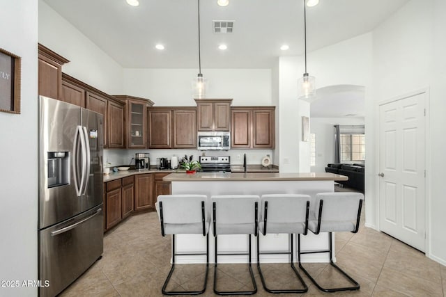 kitchen with visible vents, arched walkways, glass insert cabinets, appliances with stainless steel finishes, and decorative light fixtures