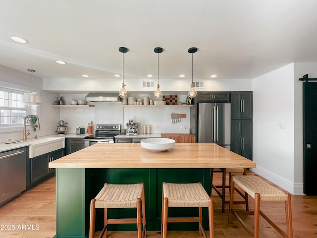 kitchen featuring wall chimney exhaust hood, appliances with stainless steel finishes, sink, and pendant lighting