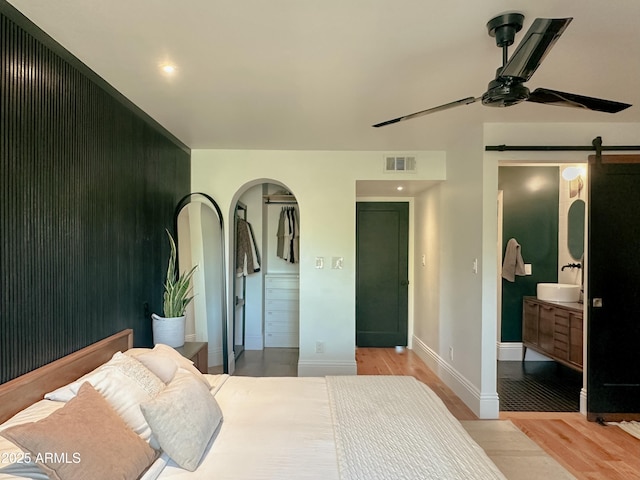 bedroom featuring ceiling fan, a barn door, sink, and light hardwood / wood-style flooring