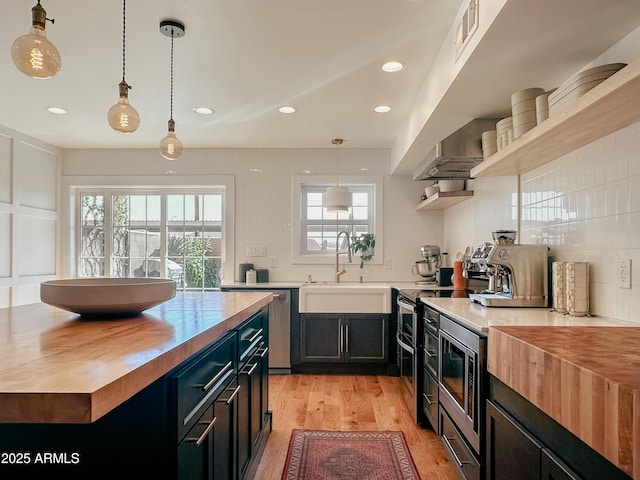 kitchen with sink, butcher block countertops, hanging light fixtures, light wood-type flooring, and stainless steel appliances