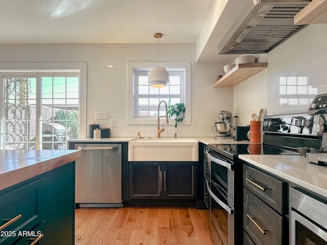 kitchen with sink, decorative light fixtures, light wood-type flooring, stainless steel appliances, and wall chimney range hood