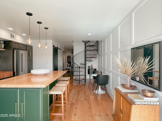 kitchen featuring high quality fridge, pendant lighting, green cabinetry, a barn door, and light wood-type flooring