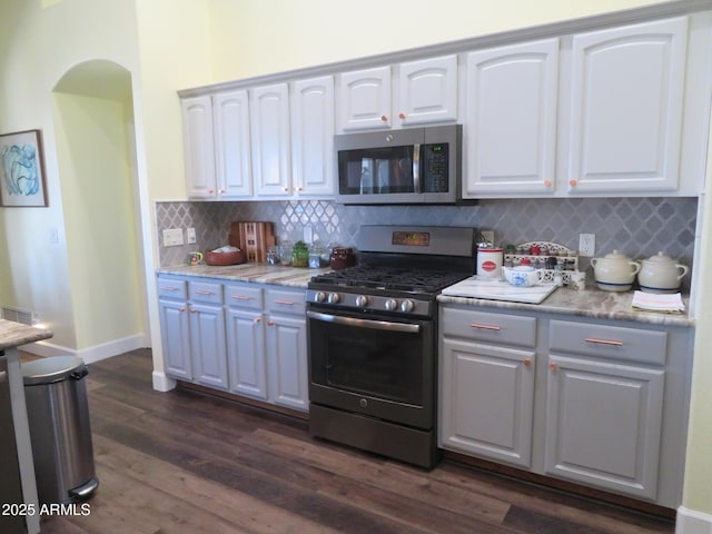 kitchen with dark wood-style floors, tasteful backsplash, appliances with stainless steel finishes, white cabinetry, and baseboards