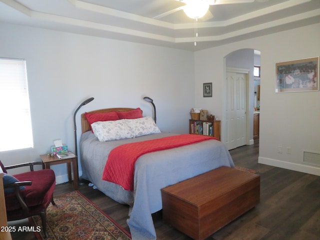 bedroom featuring a tray ceiling, arched walkways, visible vents, wood finished floors, and baseboards