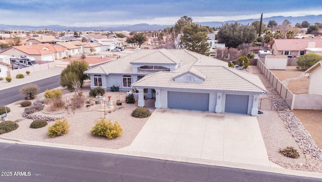 view of front facade with a tile roof, concrete driveway, fence, a mountain view, and a residential view