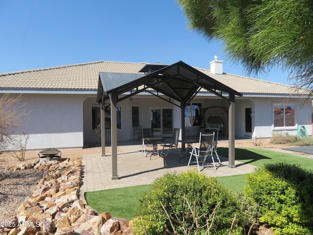 rear view of property featuring a patio area, a tile roof, a chimney, and stucco siding