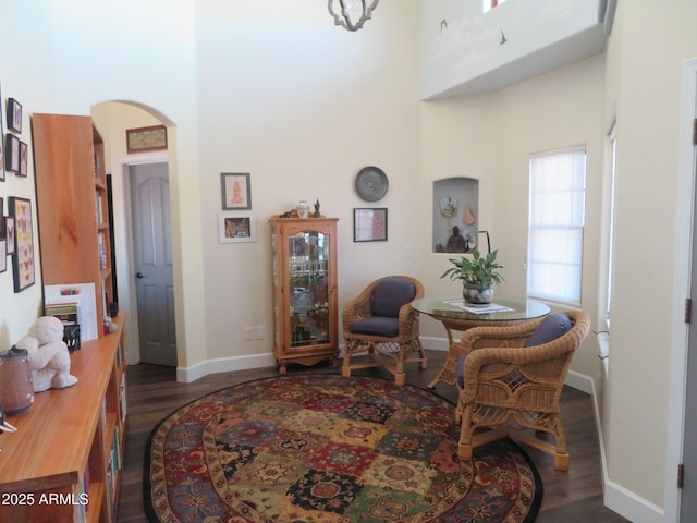 living area with a towering ceiling, baseboards, arched walkways, and wood finished floors