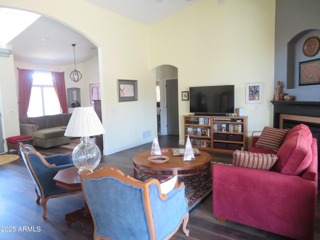 living area with arched walkways, a fireplace, visible vents, wood finished floors, and baseboards