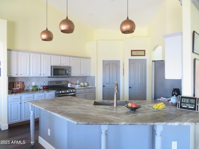 kitchen featuring white cabinets, a breakfast bar area, a peninsula, stainless steel appliances, and high vaulted ceiling