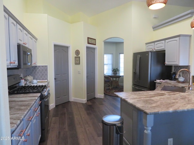 kitchen featuring arched walkways, light stone counters, stainless steel appliances, a sink, and dark wood-style floors