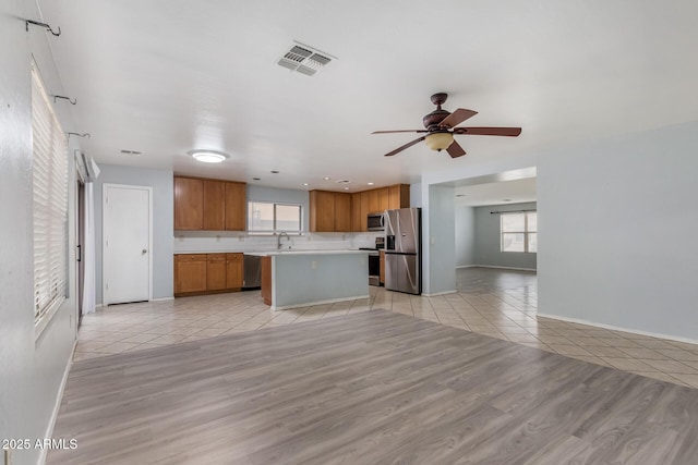 kitchen with ceiling fan, sink, stainless steel appliances, light hardwood / wood-style flooring, and a kitchen island