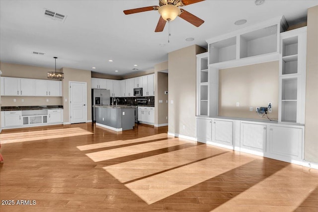 unfurnished living room with built in shelves, sink, ceiling fan with notable chandelier, and light hardwood / wood-style floors