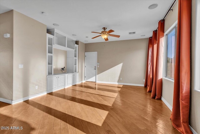 unfurnished living room with wood-type flooring, built in features, and ceiling fan