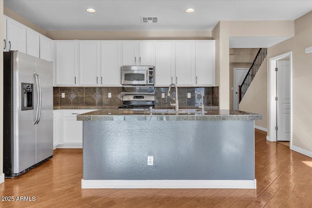 kitchen featuring tasteful backsplash, stainless steel appliances, light hardwood / wood-style floors, and white cabinets