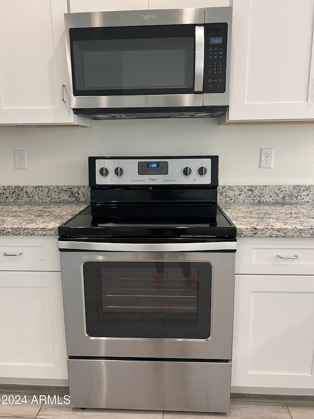 kitchen with light stone countertops, appliances with stainless steel finishes, and white cabinetry