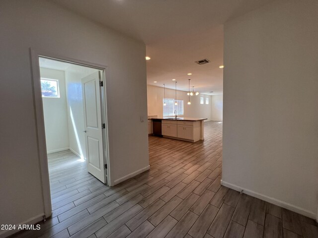 hallway with light wood-type flooring, sink, and an inviting chandelier