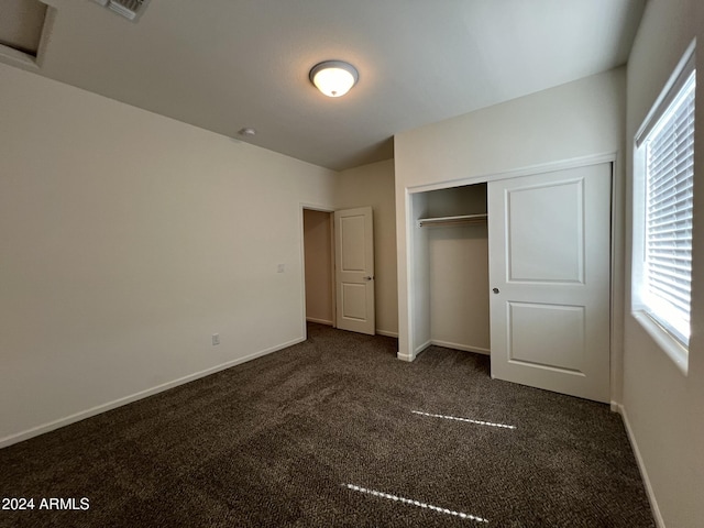 unfurnished bedroom with dark colored carpet and a closet