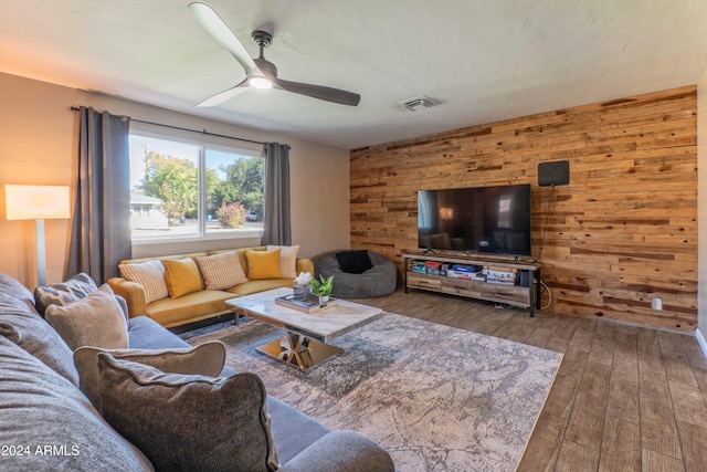 living area featuring a ceiling fan, wood walls, visible vents, and hardwood / wood-style flooring