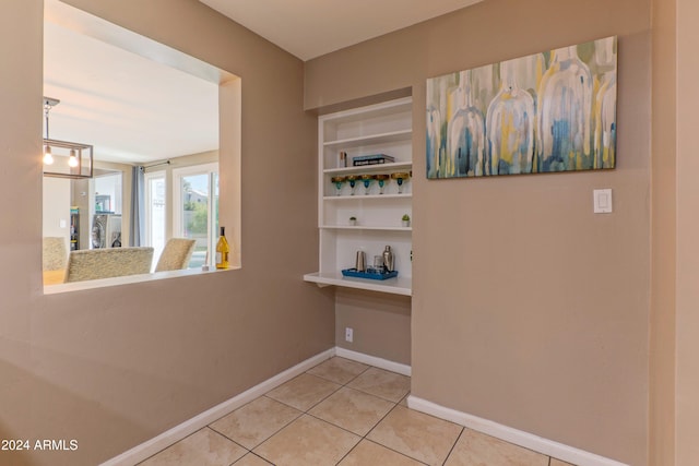 hall featuring built in shelves, light tile patterned flooring, and baseboards