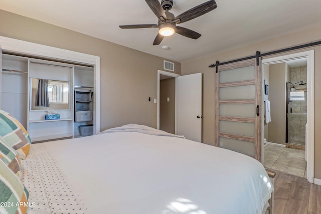 bedroom with a barn door, visible vents, a ceiling fan, wood finished floors, and a closet