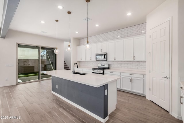 kitchen with a center island with sink, stainless steel appliances, decorative backsplash, a sink, and wood finished floors