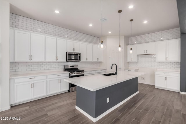 kitchen with wood finished floors, appliances with stainless steel finishes, a sink, and white cabinets